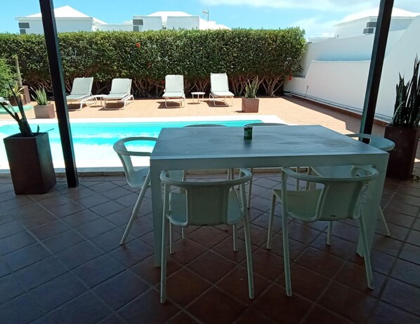 Un espace aménagé au bord de la piscine, avec une table et des chaises, une piscine et des chaises longues.