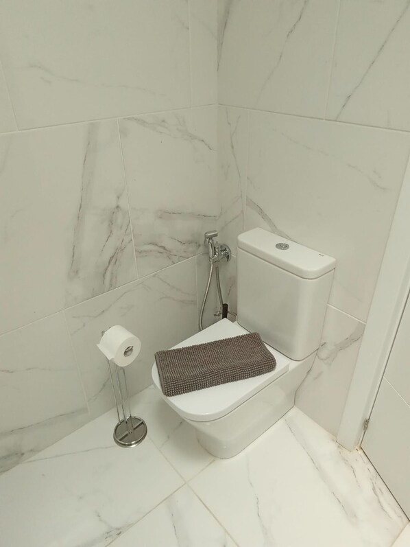 A bathroom with a toilet, a bidet, and a toilet paper holder.
