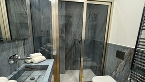 Une salle de bain moderne dotée d’une douche à parois de verre, d’une baignoire sur pieds et d’un meuble-lavabo avec un plan de travail en marbre.
