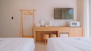 Habitación de hotel con dos camas, un escritorio de madera con microondas, televisión y perchero.