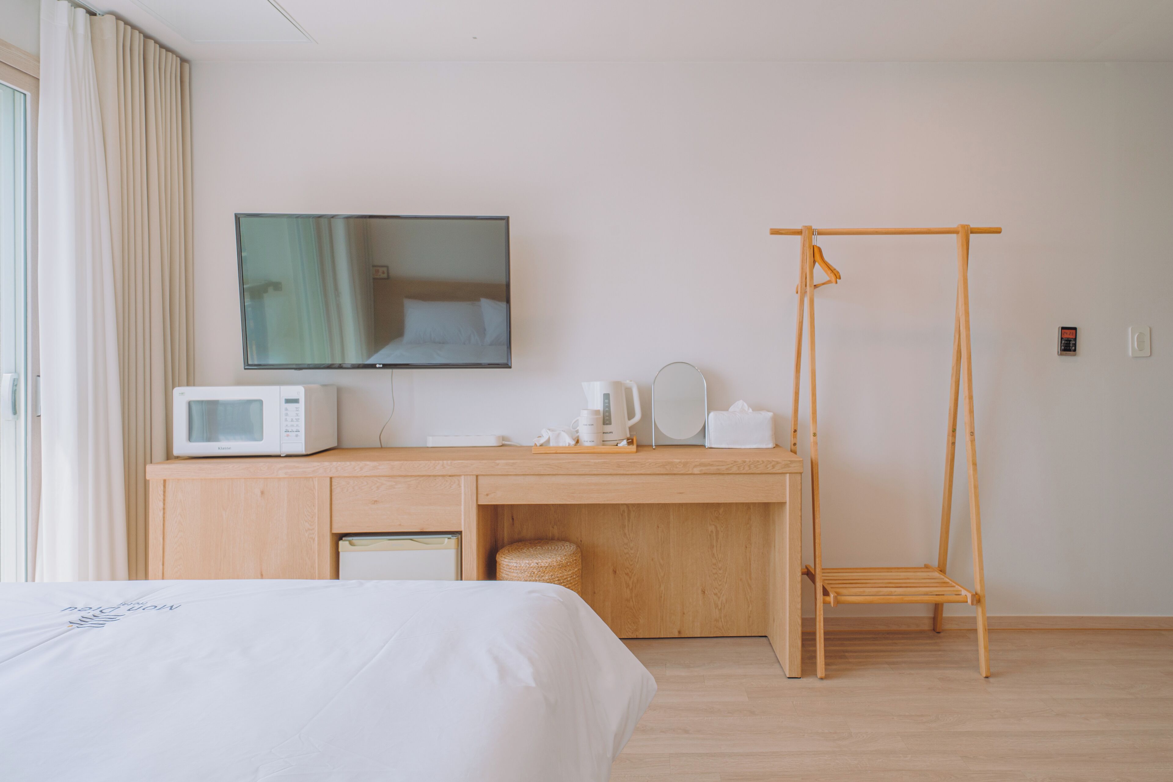Habitación de hotel con una cama, un escritorio de madera con microondas, una silla colgante y un espejo grande.