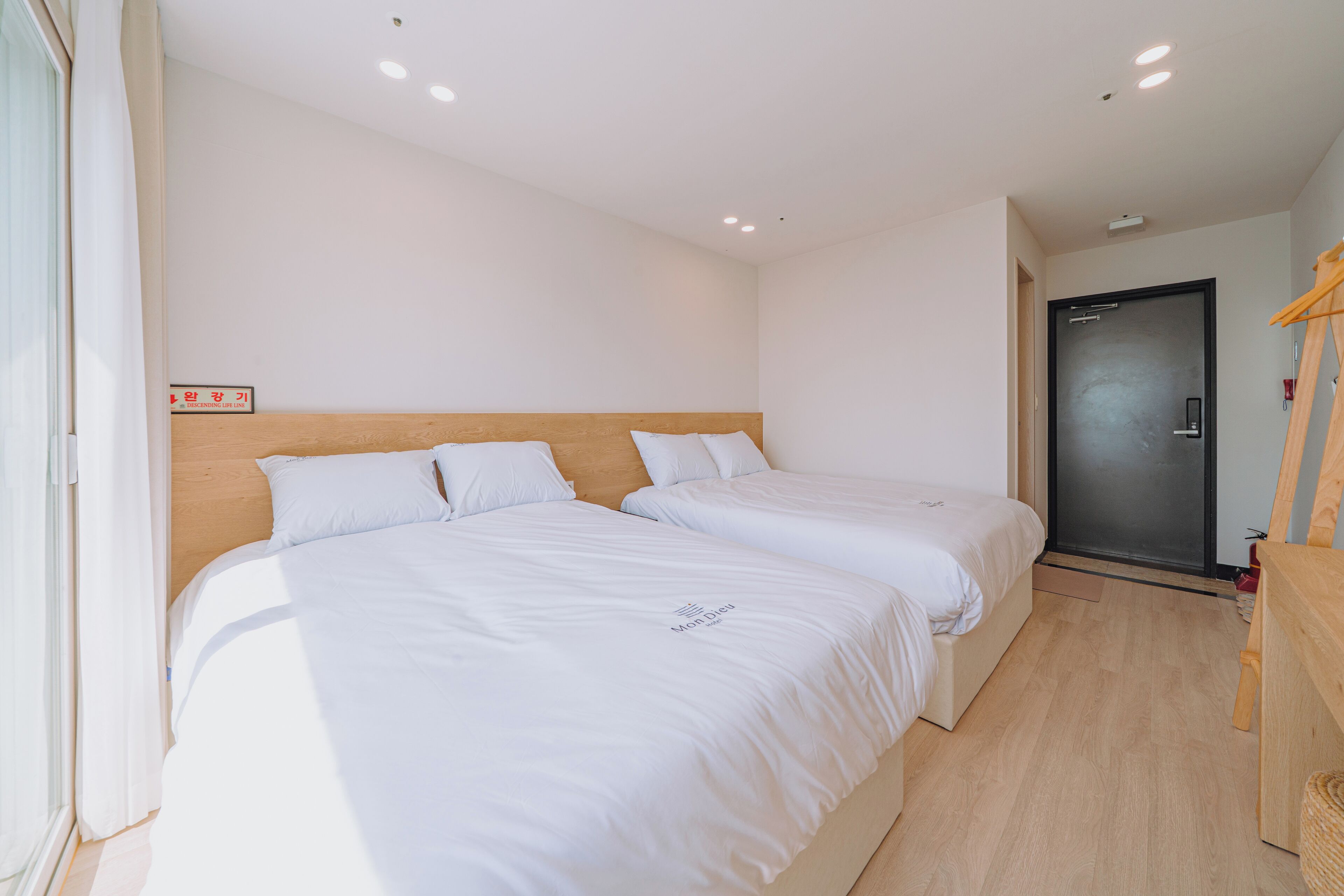 A hotel room with two beds, a wooden headboard, a dark door, and a wooden floor.