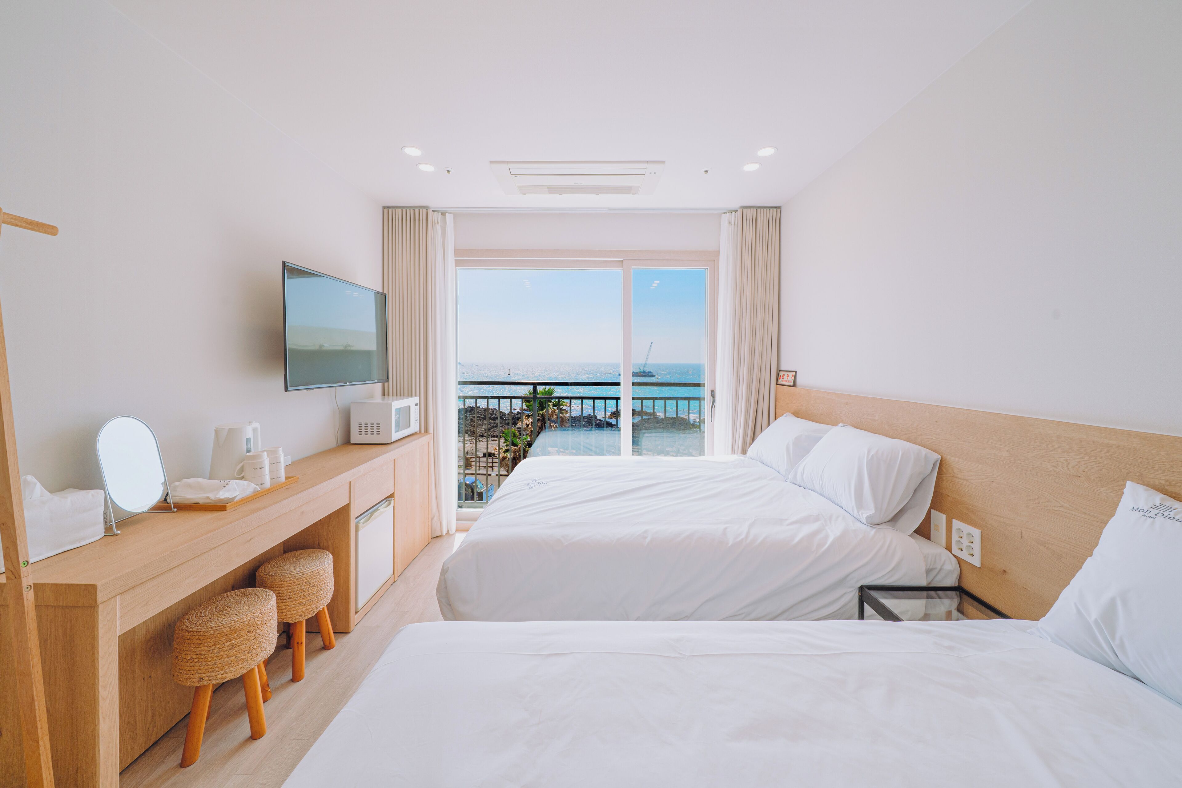Une chambre d’hôtel avec un grand lit, un bureau avec un miroir et une télévision. La fenêtre offre une vue sur la mer.