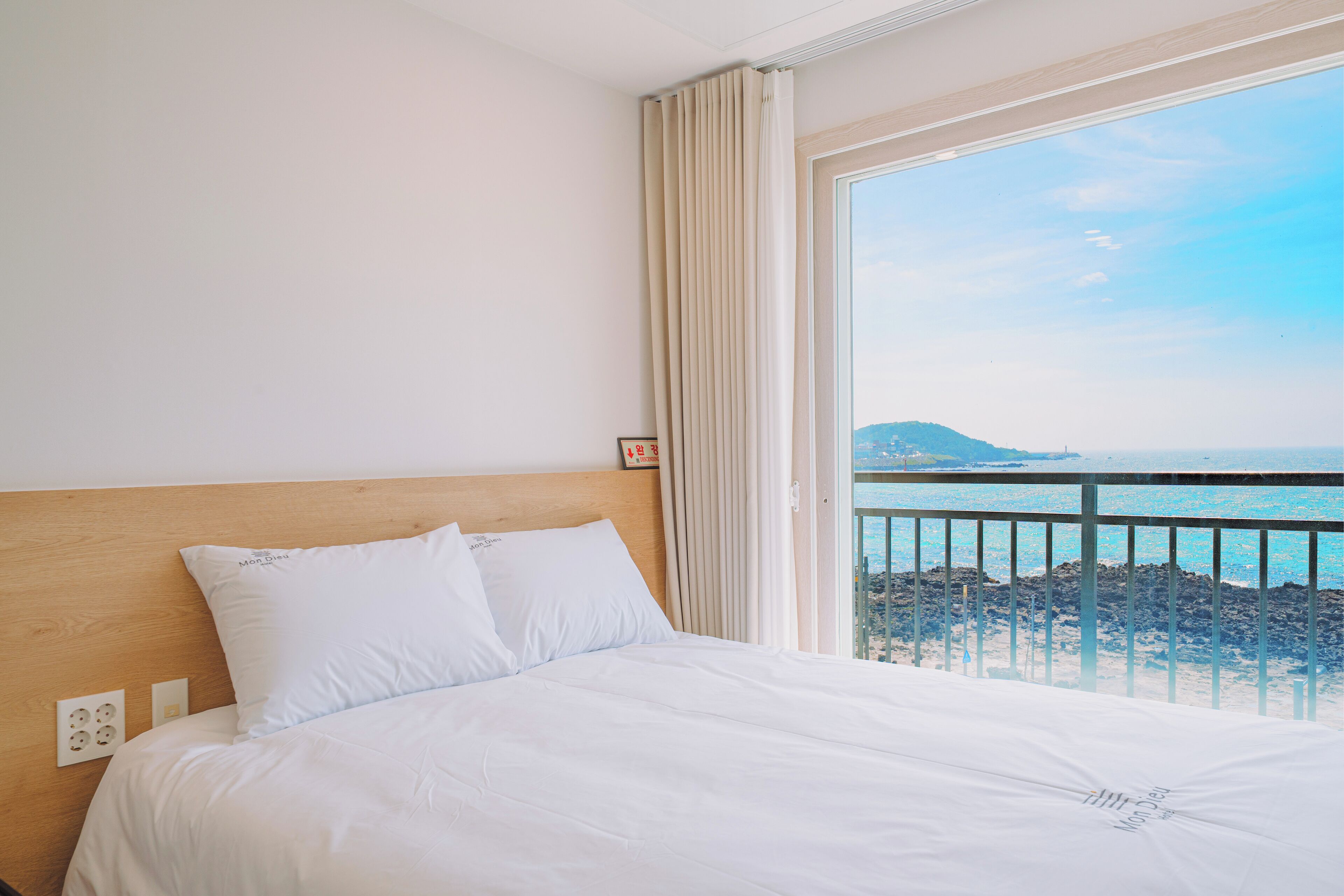 A hotel room with a bed, a view of the sea, and a balcony with a railing.