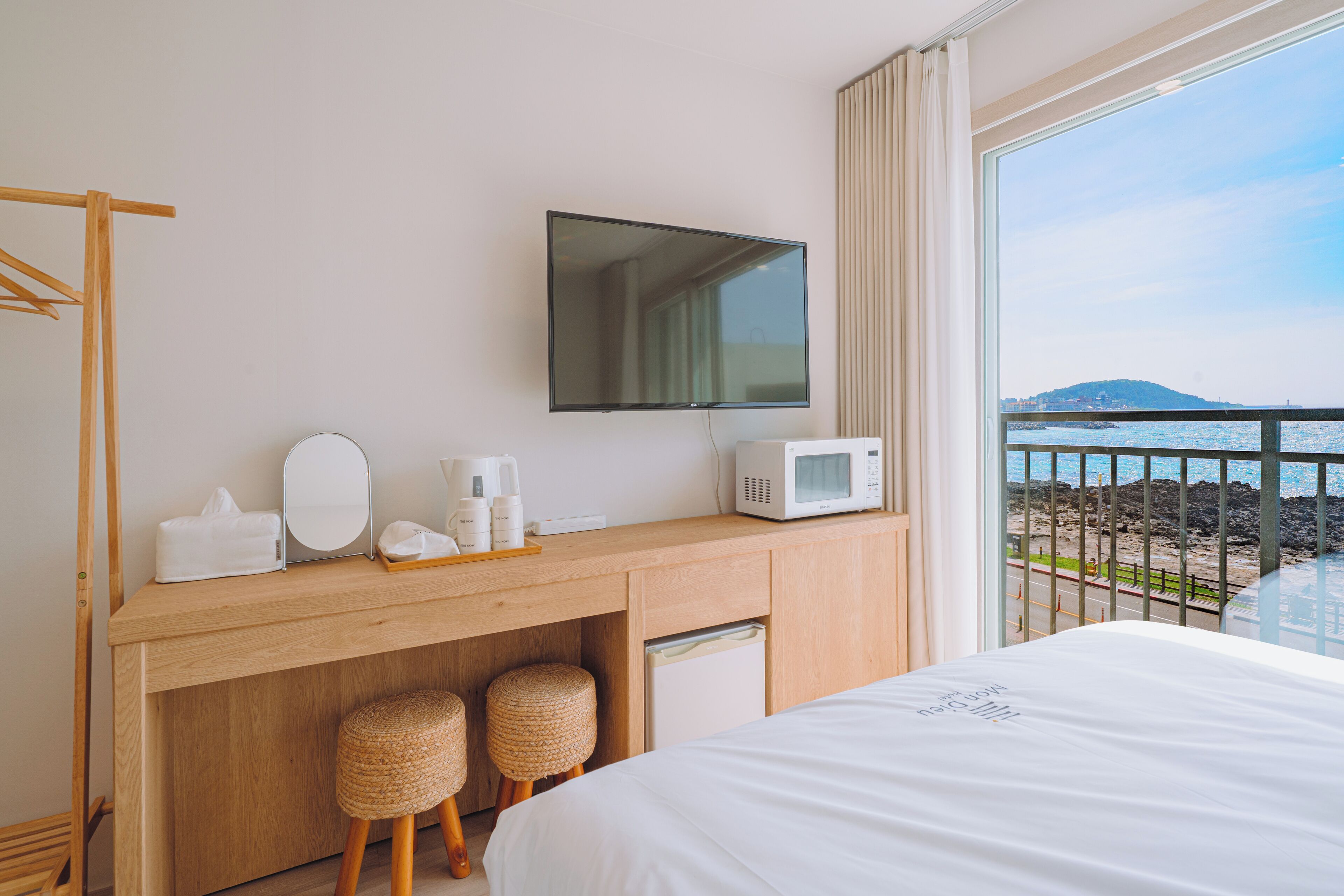 Une chambre d’hôtel dotée d’un bureau en bois, d’un téléviseur à écran plat, d’un four à micro-ondes, d’un petit réfrigérateur et d’un lit offrant une vue sur la mer.