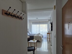 A hotel room with a bed, a bedside table, a chair, a coat rack, and a television.