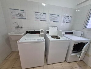 Une buanderie équipée de trois machines à laver, d’un évier et de panneaux d’affichage contenant des informations.