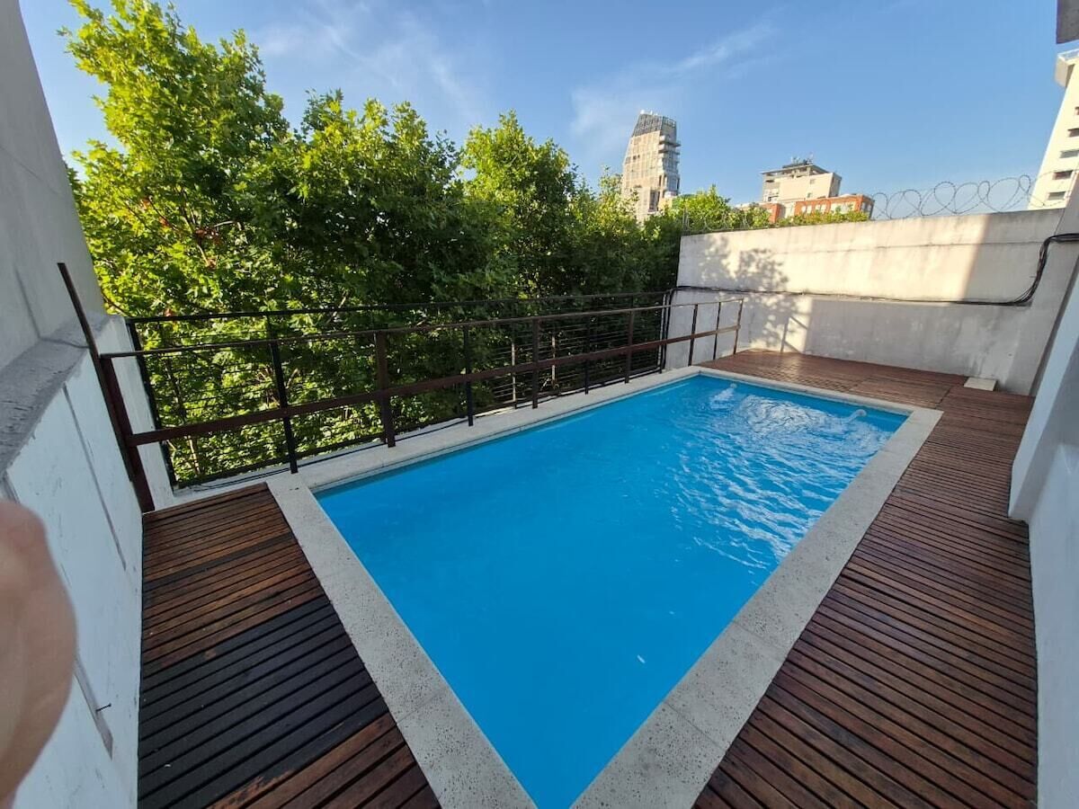 A rooftop swimming pool with a wooden deck and a metal railing.
