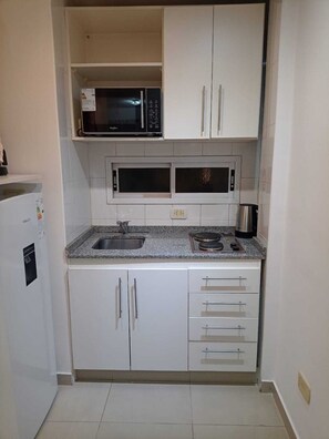 A compact kitchen with white cabinets, a granite countertop, a microwave, and a coffee maker.