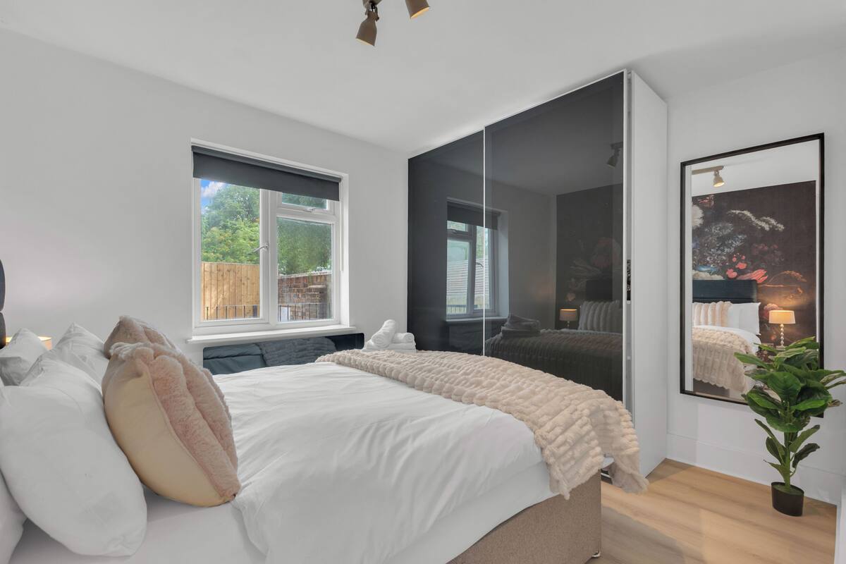 A modern bedroom with a large bed, a window, a mirror, and a potted plant.