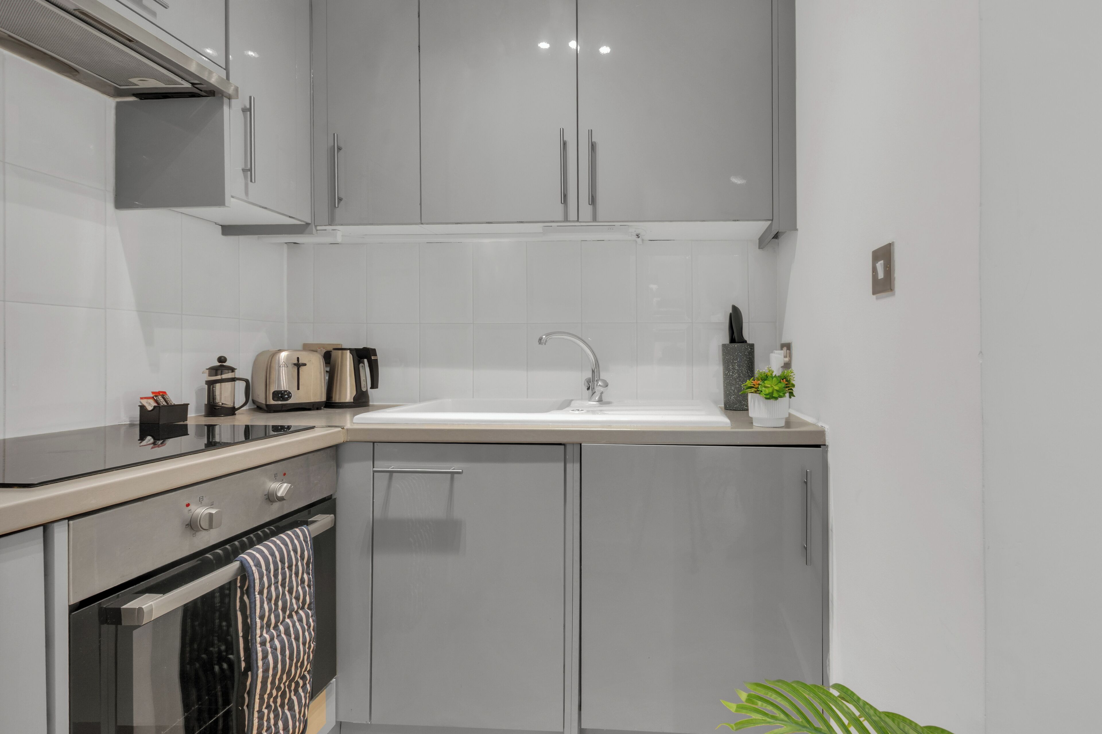 A modern kitchen with grey cabinets, a stainless steel oven, a sink, and a countertop with a kettle and toaster.