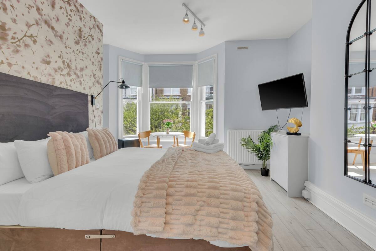 A bedroom with a large bed, a TV mounted on the wall, and a view of the outdoors through a window.