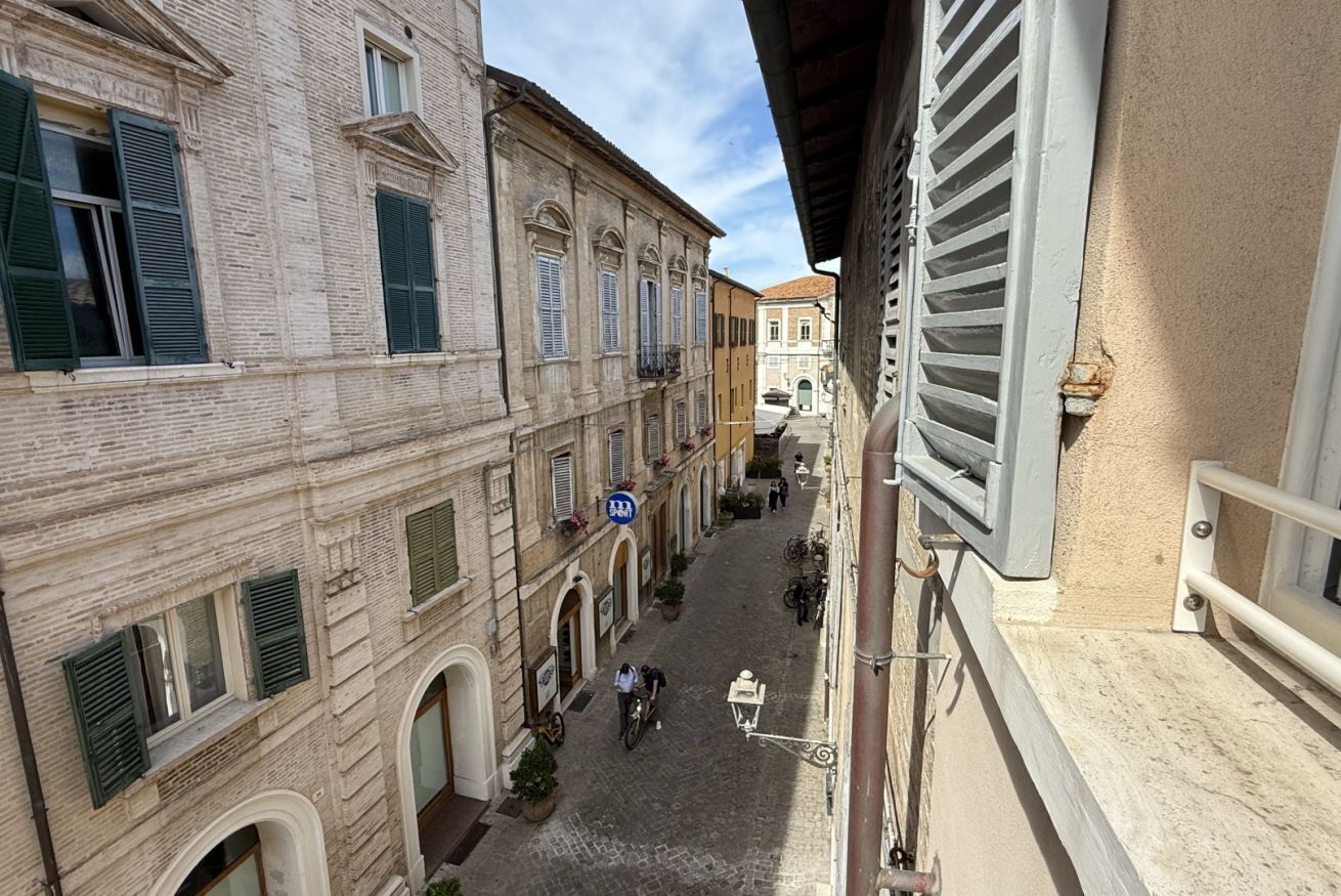 A narrow street with buildings on either side, featuring arched windows and shutters.
