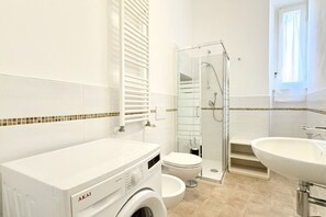 Uma casa de banho moderna com máquina de lavar roupa, sanita, cabine de duche em vidro e lavatório.