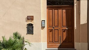 Una puerta doble de madera con un arquitrabe metálico decorativo, un buzón y una placa en la pared.