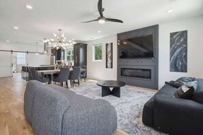 Uma sala de estar moderna com sofá, espaço de jantar com cadeiras, TV fixada na parede e ventilador de teto.