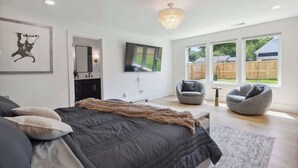 Een slaapkamer met een bed, een televisie, een stoel en uitzicht op buiten.