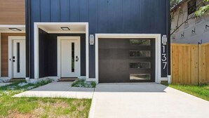 A modern building with three garage doors, a concrete pathway, and a wooden fence. - Luxury Build - King Beds - Minutes to Uptown (Charlotte)