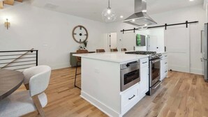 A modern kitchen with white cabinetry, a central island, stainless steel appliances, and a hanging light fixture. - Luxury Build - King Beds - Minutes to Uptown (Charlotte)