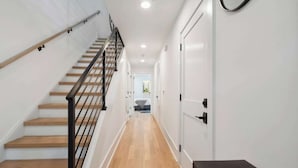A modern interior with a wooden staircase, white walls, and a hallway leading to a room. - Luxury Build - King Beds - Minutes to Uptown (Charlotte)