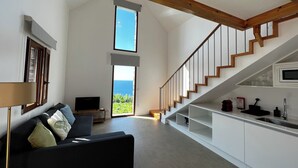 A modern interior with a sofa, TV, kitchen, and a staircase leading to a balcony with a view. - CASAS DO LARANJO- Cottages Infinity Pool by brugrani (Santa Cruz)
