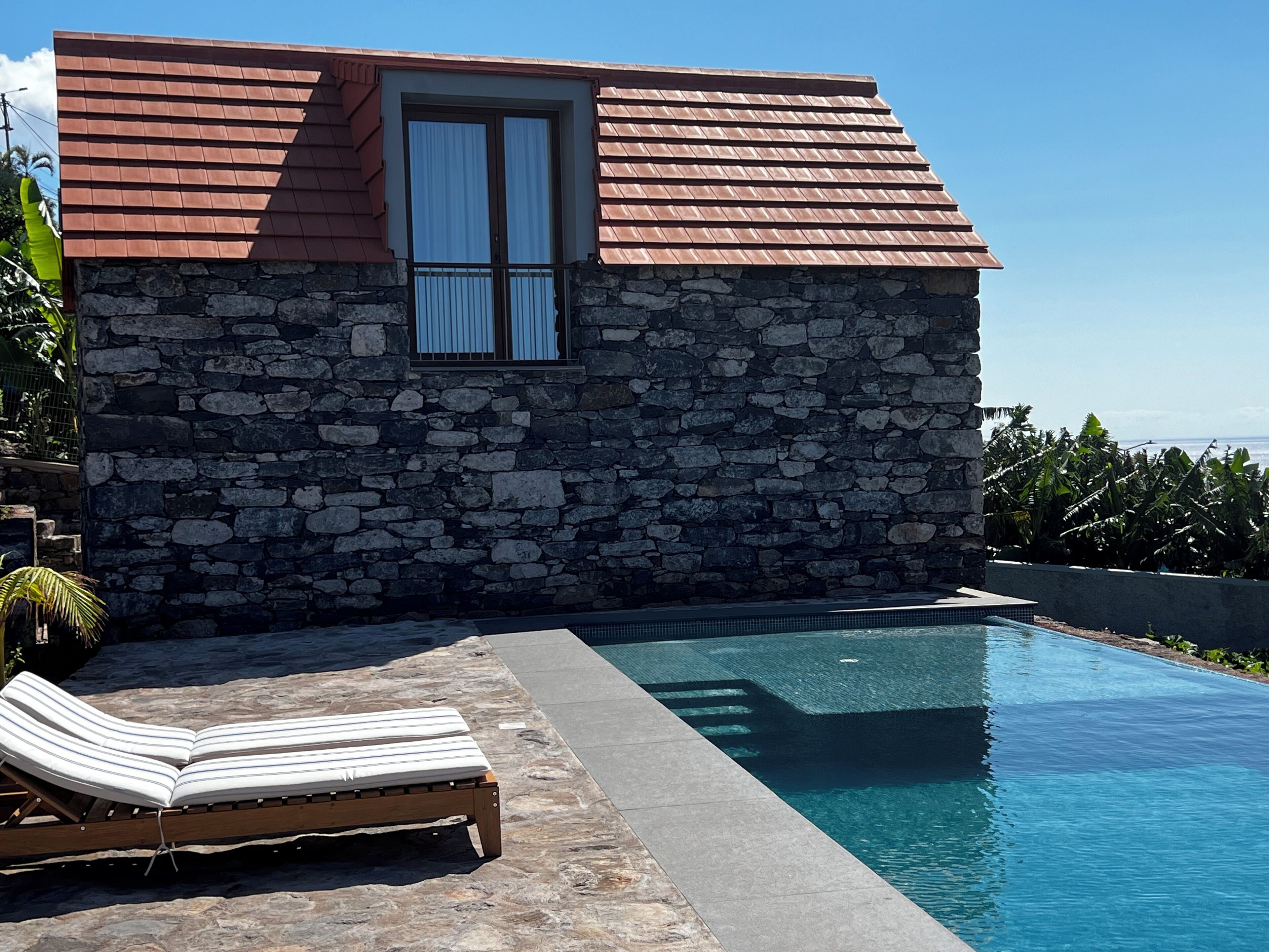 Un bâtiment en pierre avec une piscine, une fenêtre avec des rideaux et un fauteuil de relaxation.