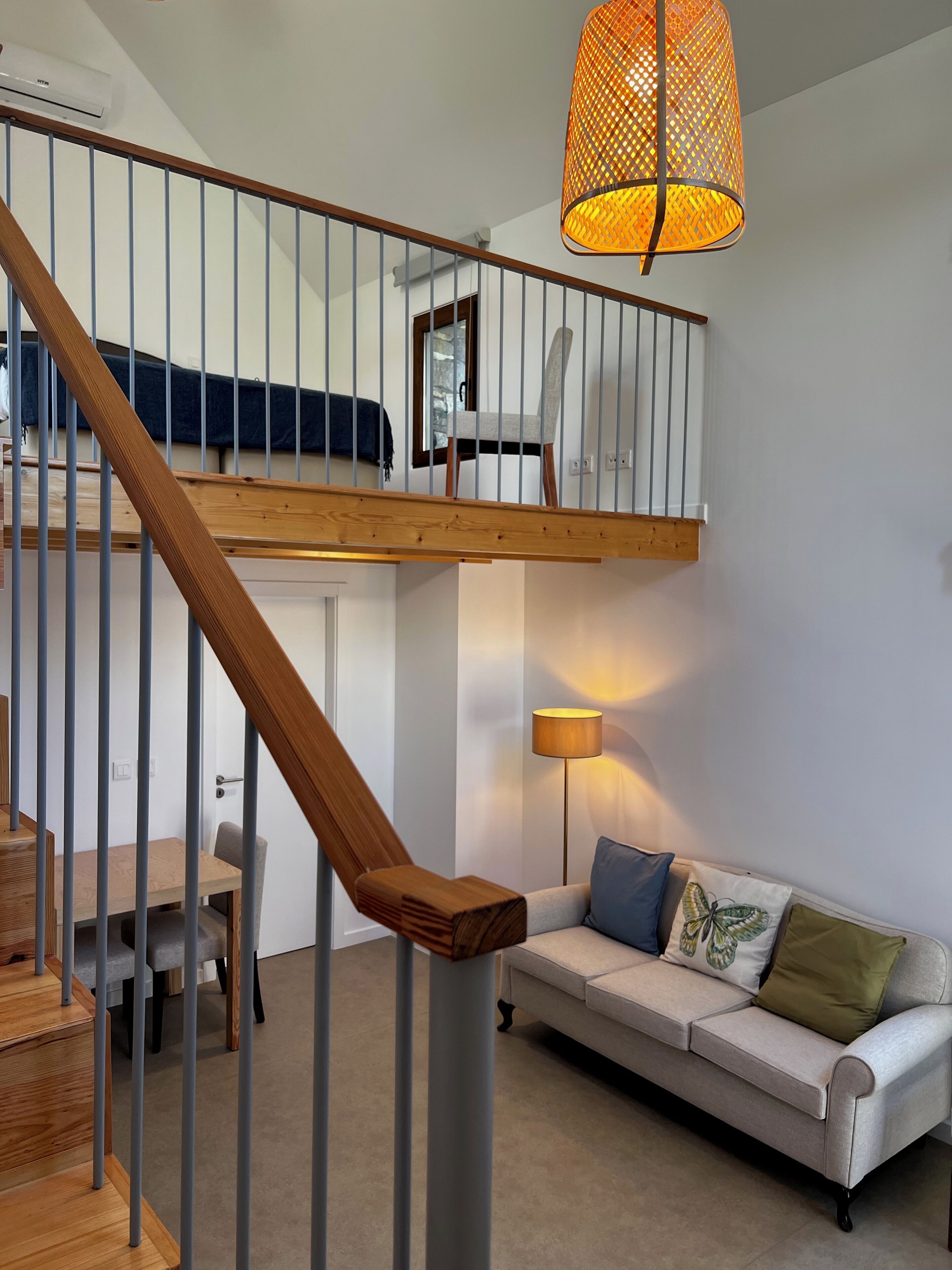A modern interior with a wooden staircase, a sofa, a lamp, and a hanging light fixture.