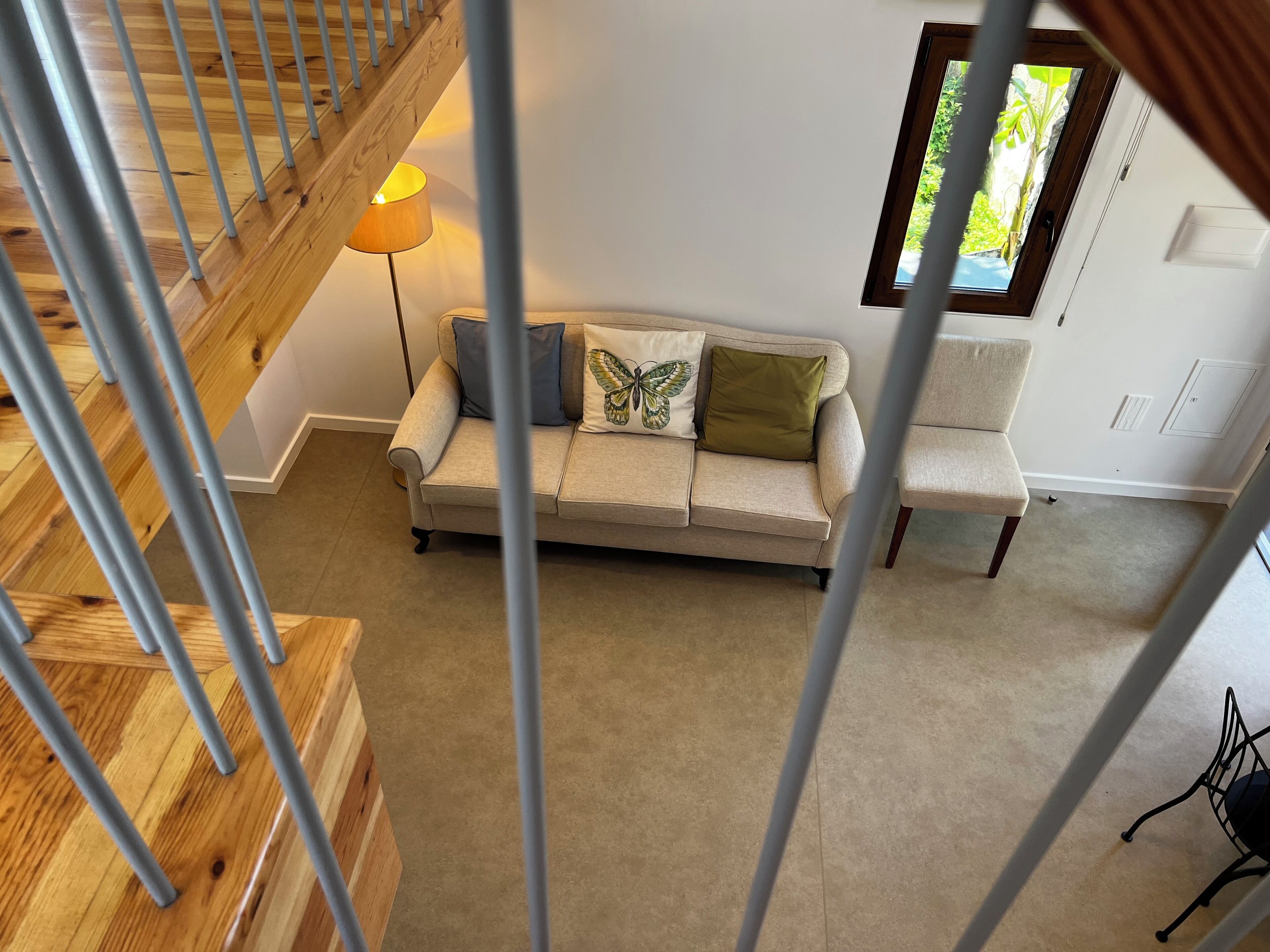 A living room with a beige sofa, a lamp, a window, and a staircase.