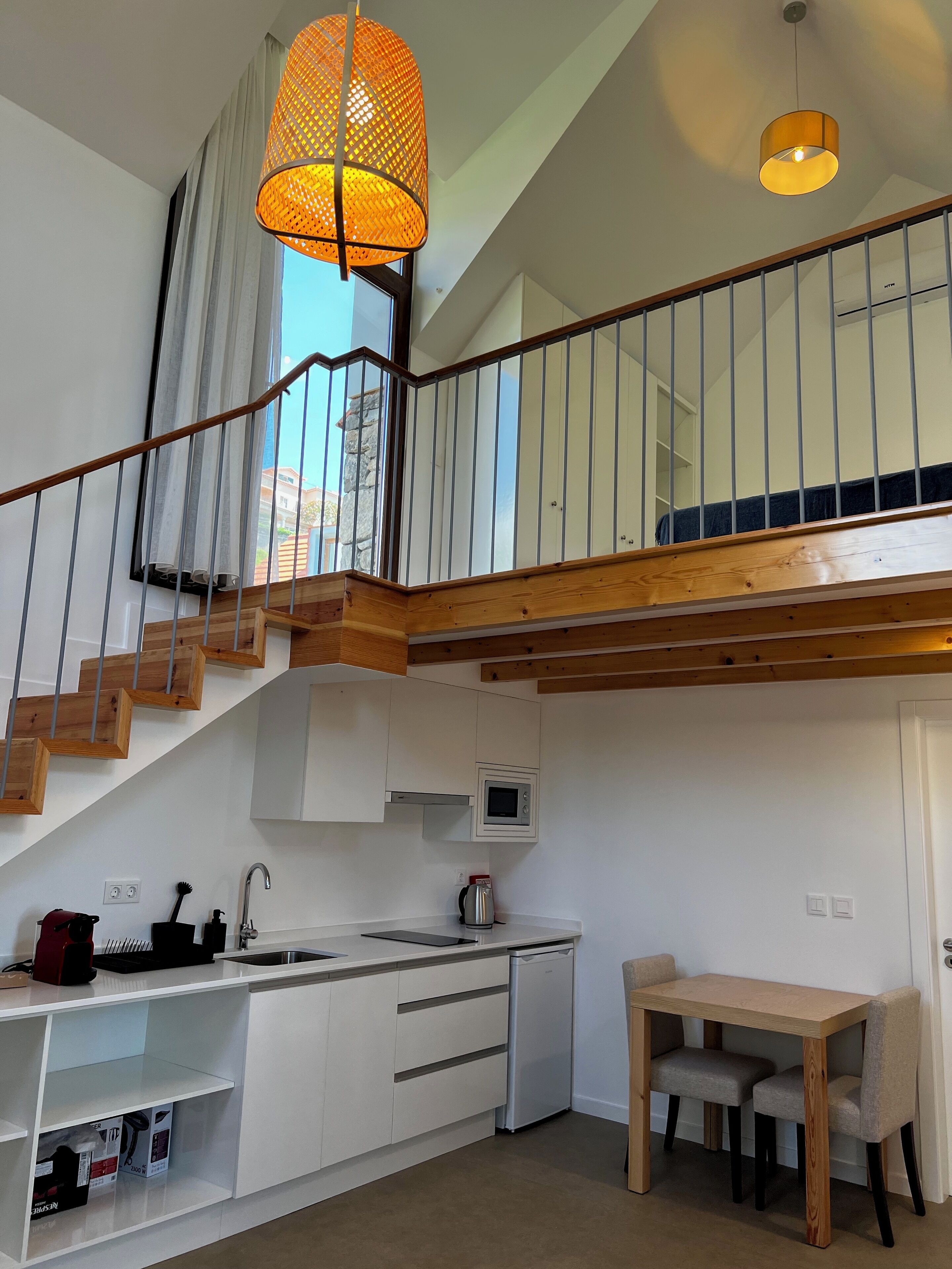 A modern kitchen with a wooden staircase, a dining area, and a view of the outside.