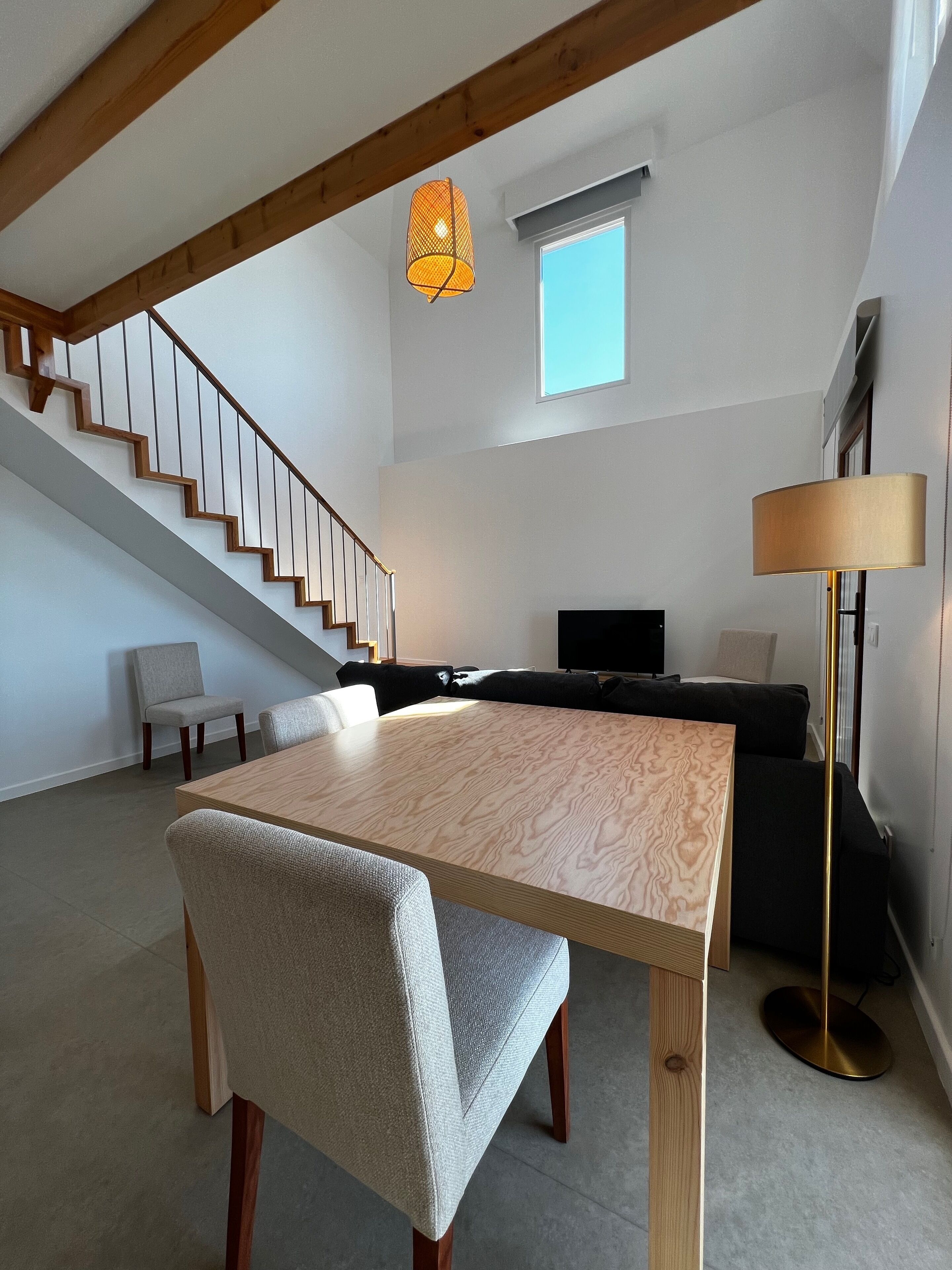 Una sala de estar moderna con una escalera de madera, una mesa de comedor y un sofá.