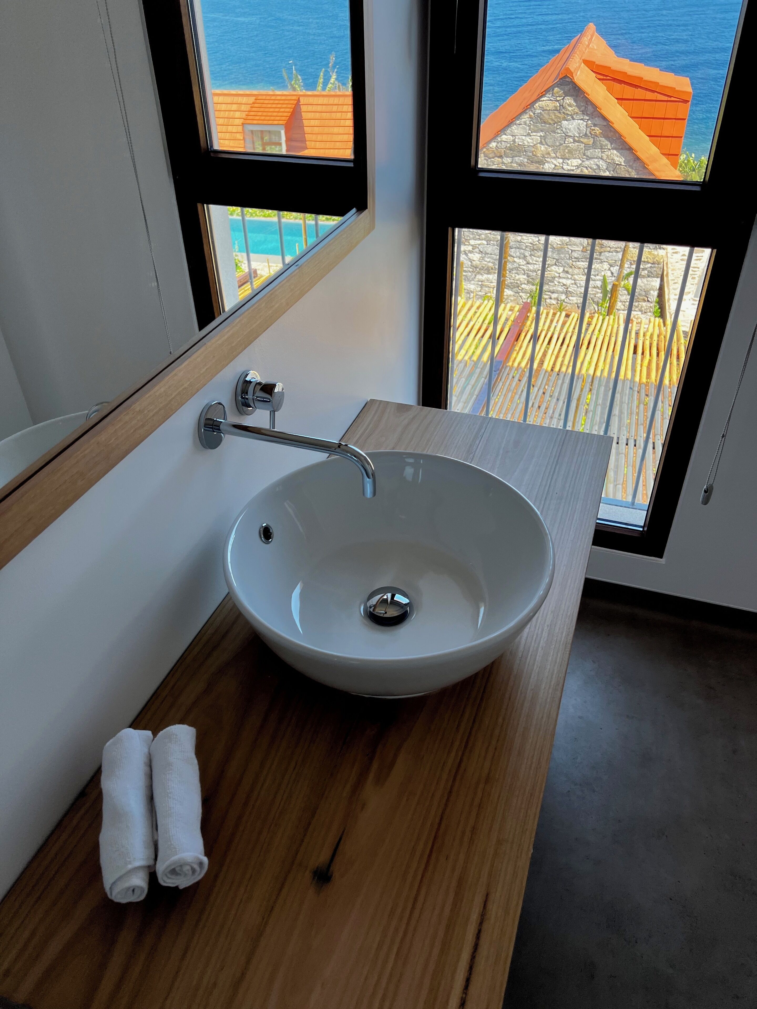 A modern bathroom with a large oval sink, wooden countertop, and two rolled towels.