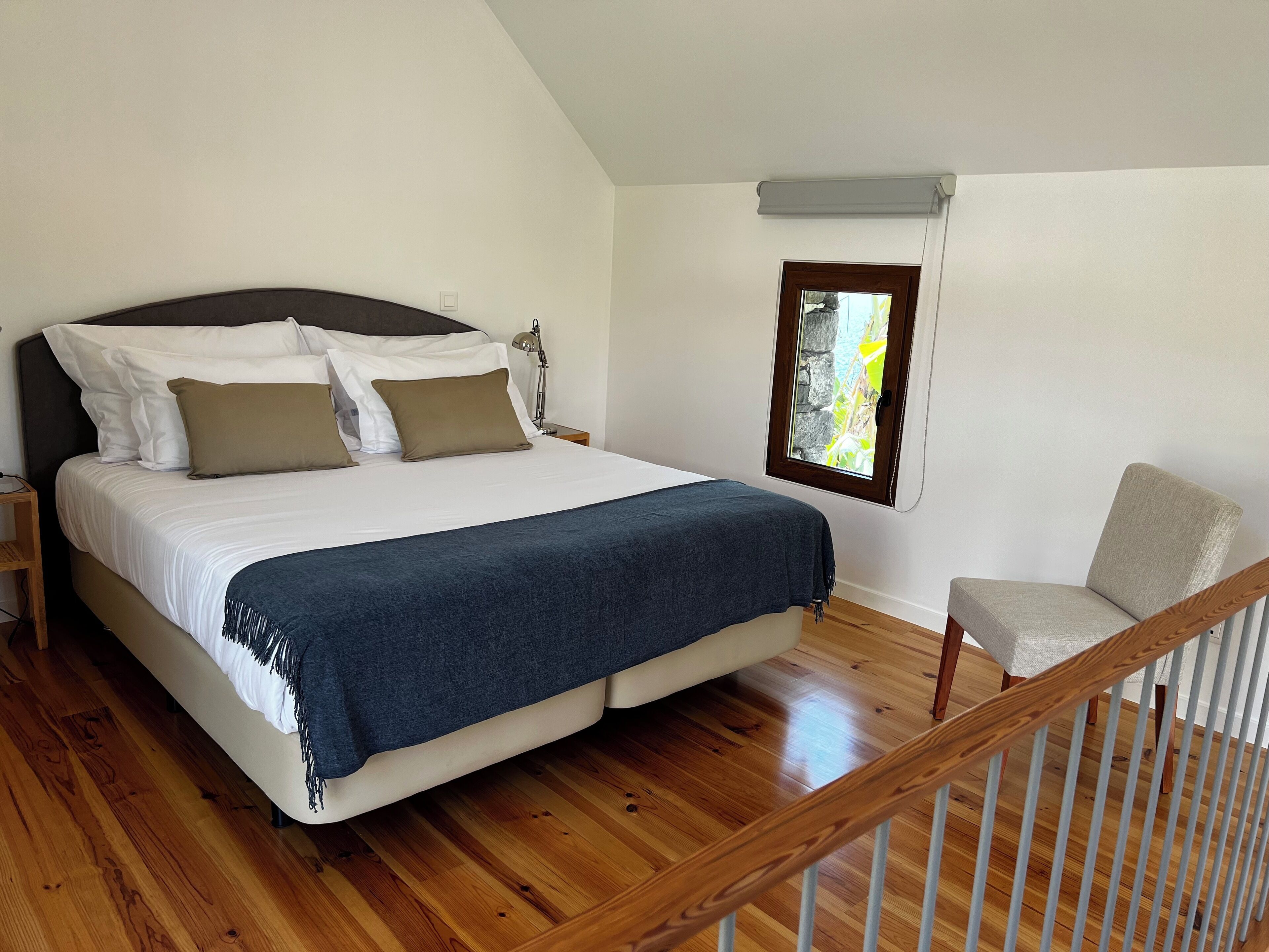 A bedroom with a bed, a chair, a nightstand, and a window.