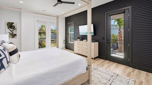 A modern bedroom with a four-poster bed, a ceiling fan, a TV, and a view of the outdoors. - Sea La Vie: Private Beach, Golfcart, Heated Pool & Hot Tub, Game Room, Bunk Room (Miramar Beach)