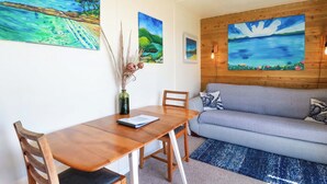 A dining area with a wooden table and chairs, a grey sofa, and three landscape paintings on the wall. - The Studio (Truro)