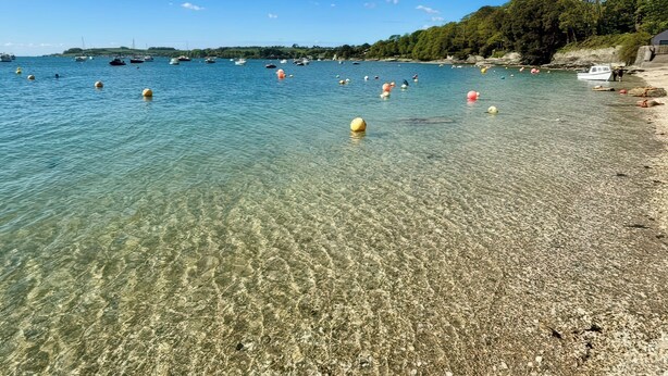 A clear beach with boats and buoys, rocky shoreline, and trees. - The Studio (Truro)