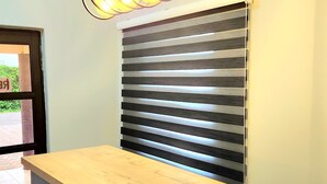 A reception desk with a wooden top and black drawers, a modern light fixture with exposed bulbs, and a window with horizontal blinds.