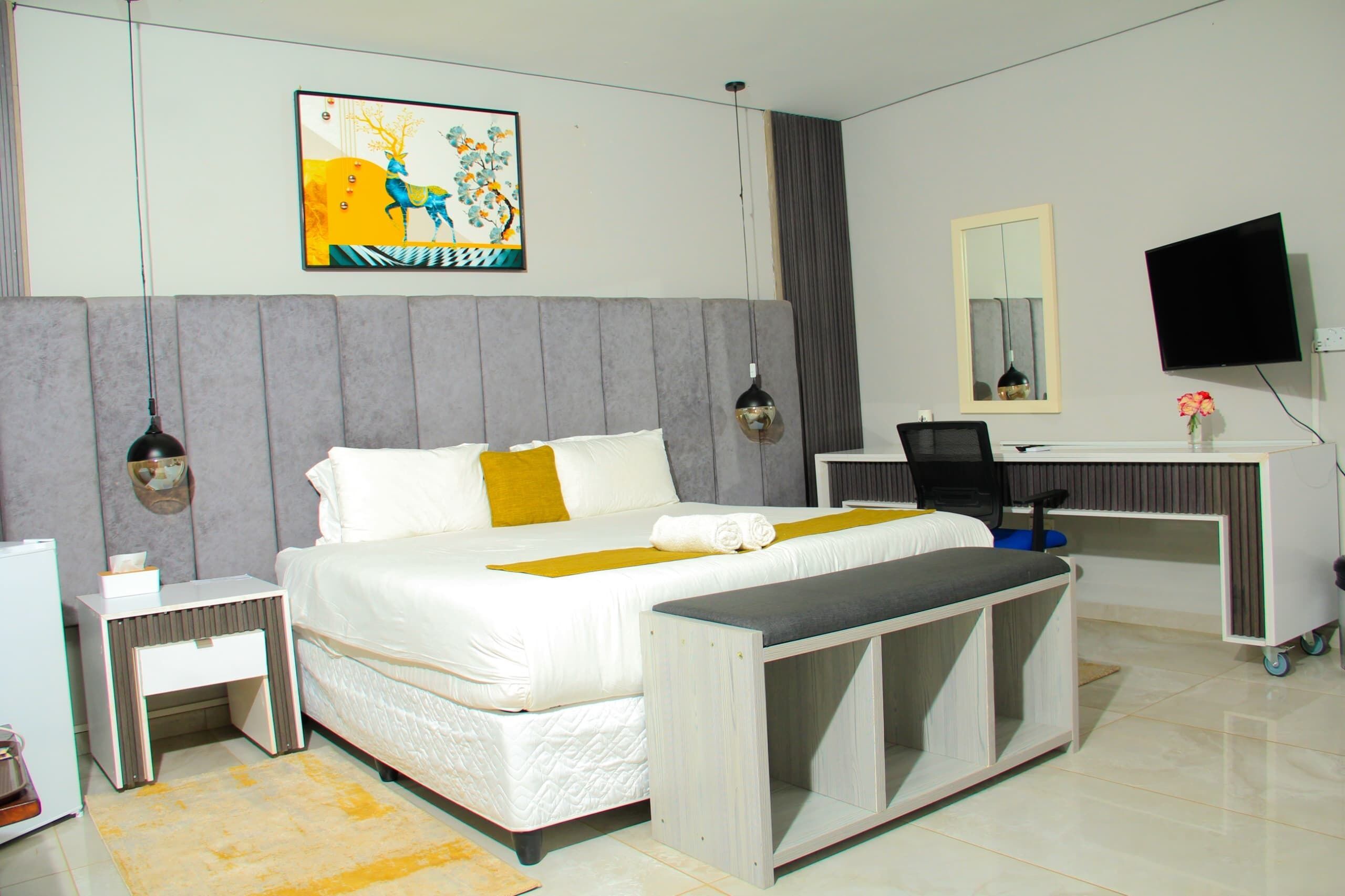 A modern hotel room with a large bed, a desk, a chair, a TV, and a painting on the wall.