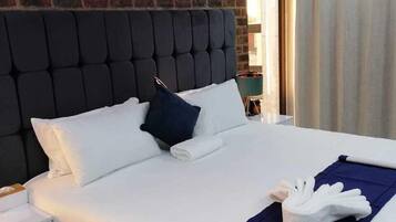 Habitación de hotel moderna con pared de ladrillo, cabecera capitonada, ropa de cama blanca y almohada decorativa azul.