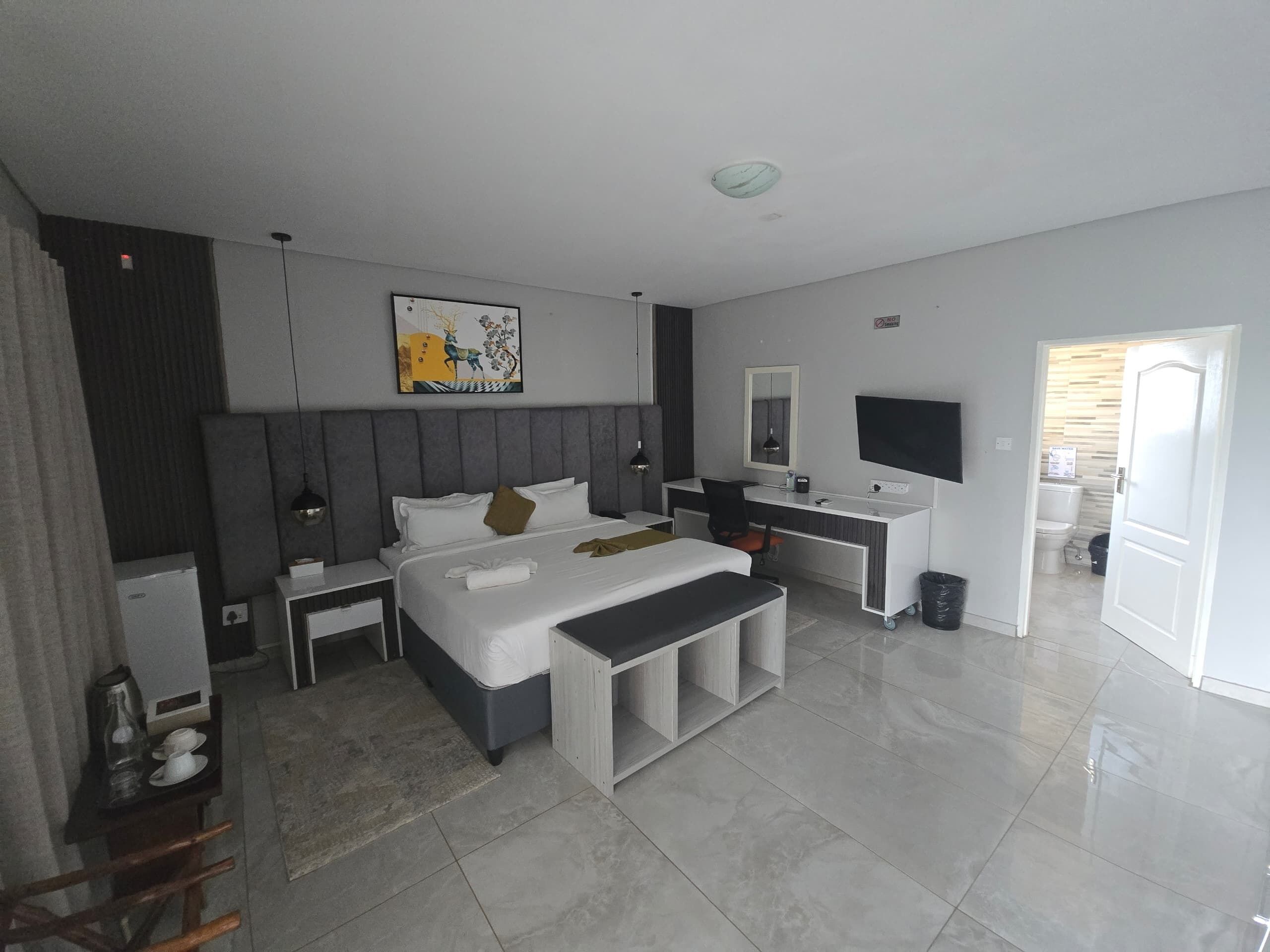 Une chambre d’hôtel moderne, dotée d’un grand lit, de tables de chevet, d’un bureau avec une chaise, d’une télévision et d’une salle de bain visible à travers une porte ouverte.