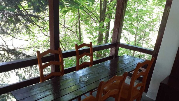 A wooden table with four chairs, set on a balcony with a view of trees. - Pensiunea Szurdok - Antonia Panzió (Baile Tusnad)