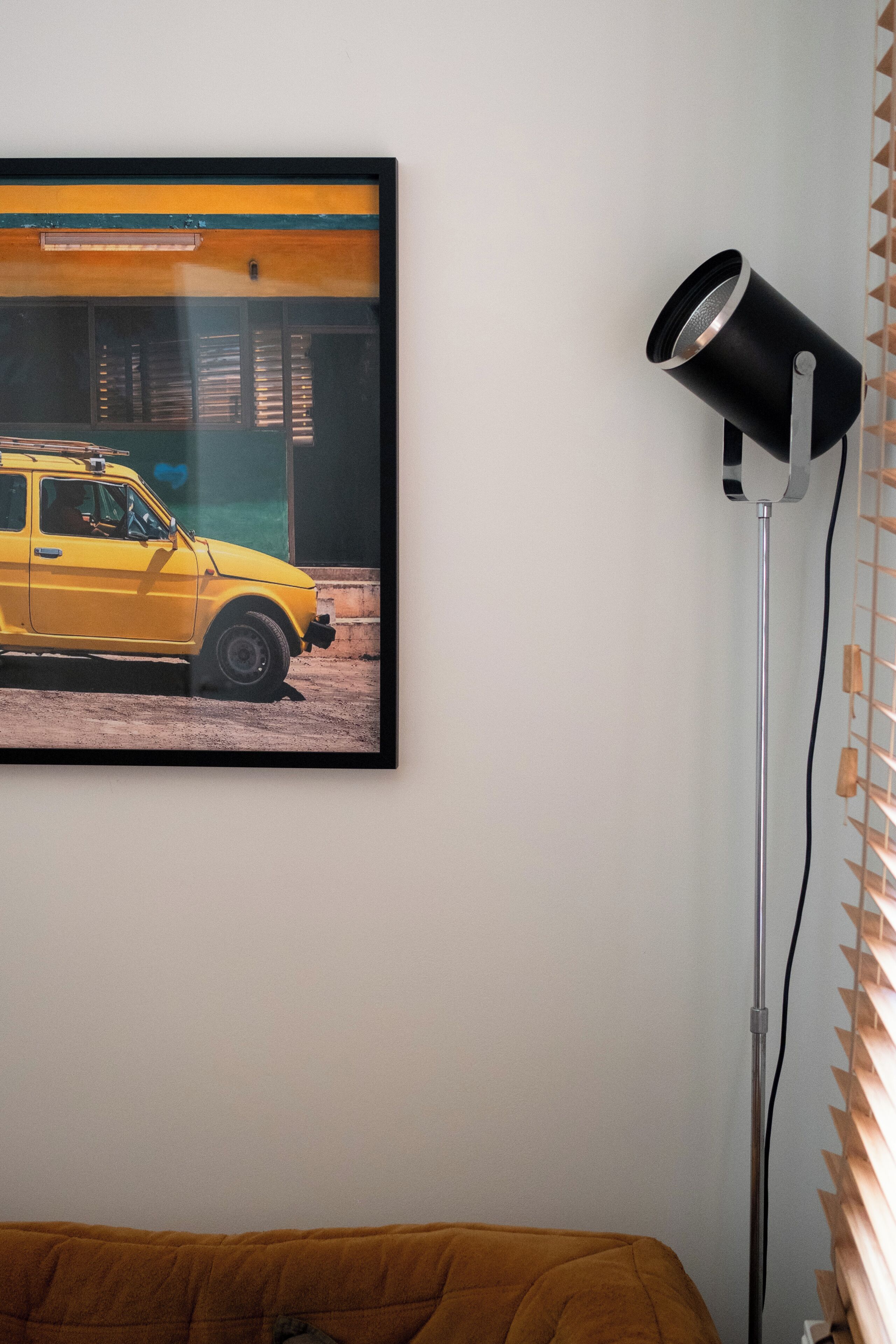 Un cuadro con un coche amarillo en una pared, una lámpara de pie negra y un sofá marrón.