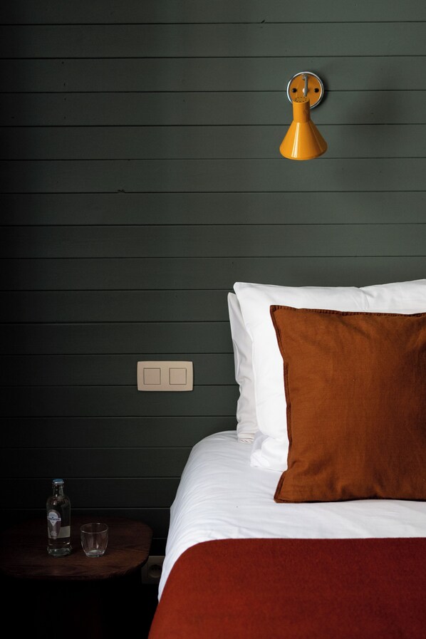 A hotel room with a bed, a nightstand, a bottle, and a glass.