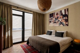 A hotel room with a large bed, a view through a sliding door, a woven ceiling light, and a family photo on the wall.