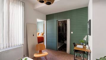 A compact room with a bed, a desk with a chair, a radiator, and a window with blinds.