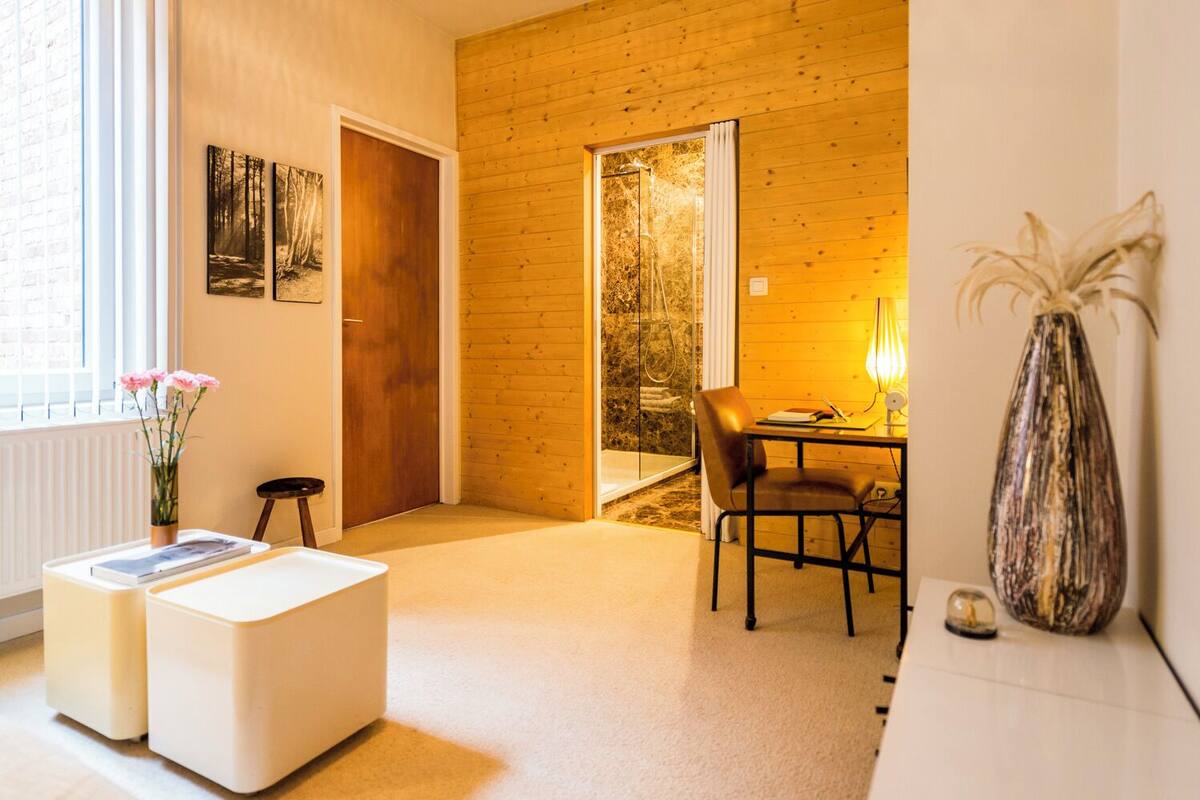 Ein modernes Zimmer mit Holzboden, einer Glasdusche, einem Esstisch mit Stühlen, einem weißen Sofa und einer Vase mit Blumen.