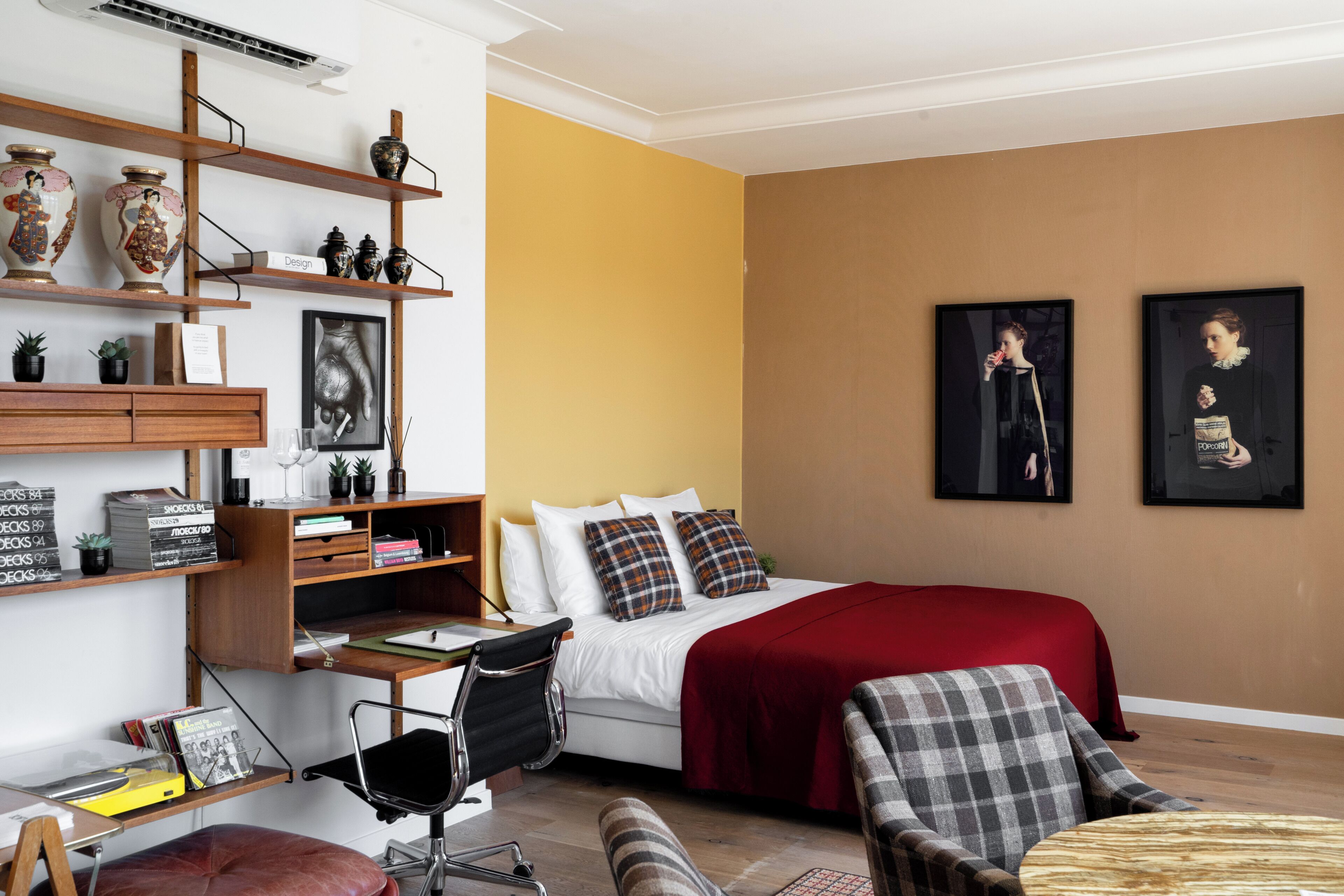 Ein modernes Schlafzimmer mit einem Bett, einem Schreibtisch, Regalen mit Dekoration und zwei gerahmten Bildern an der Wand.