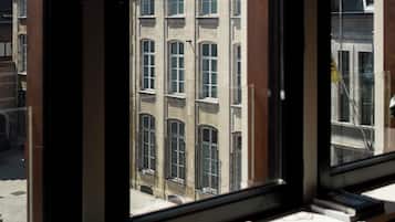 A view through a window with a radiator below, a book on the windowsill, and a building with multiple windows and a bell tower in the background.