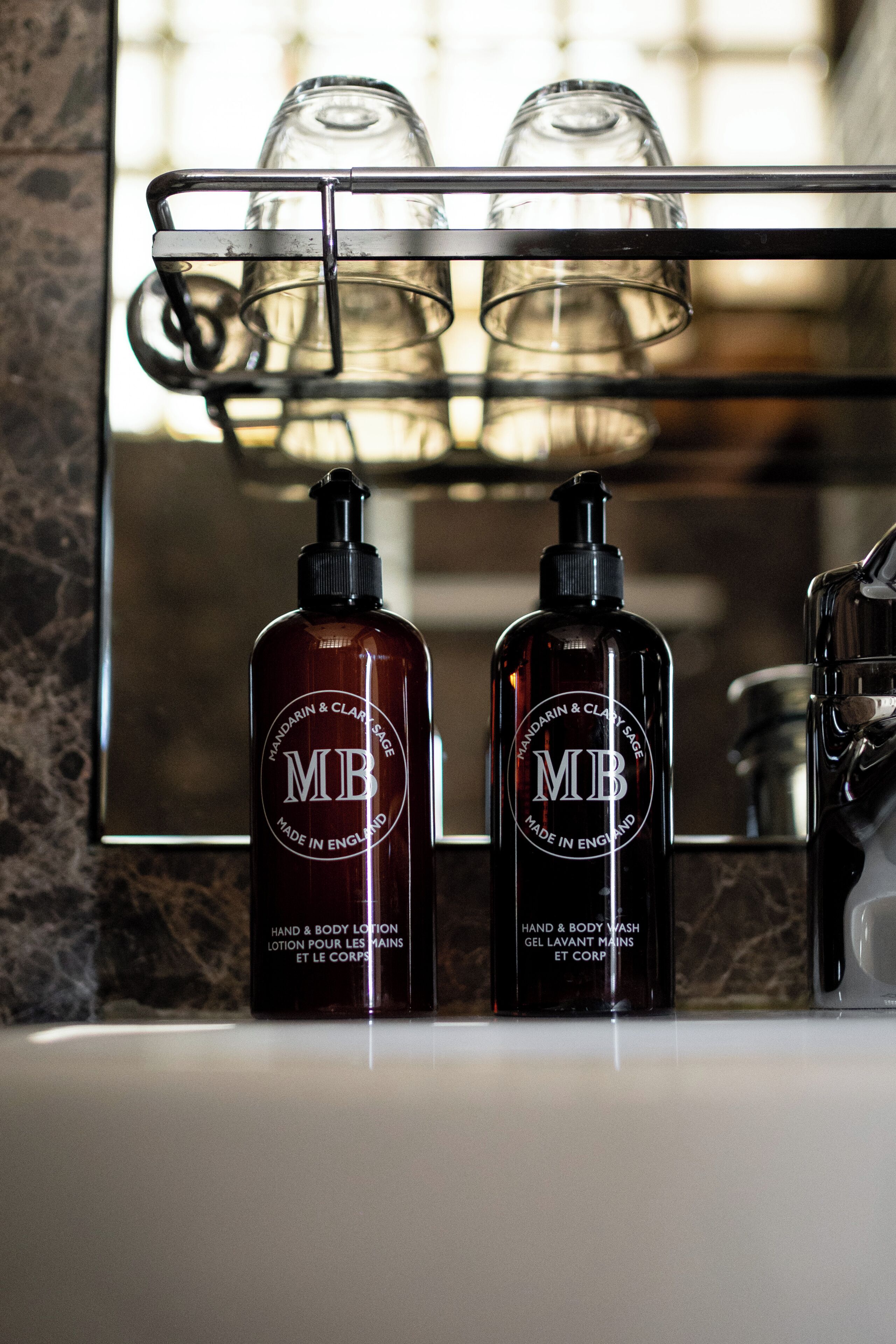 Two bottles of hand and body lotion on a bathroom counter with a mirror above them.