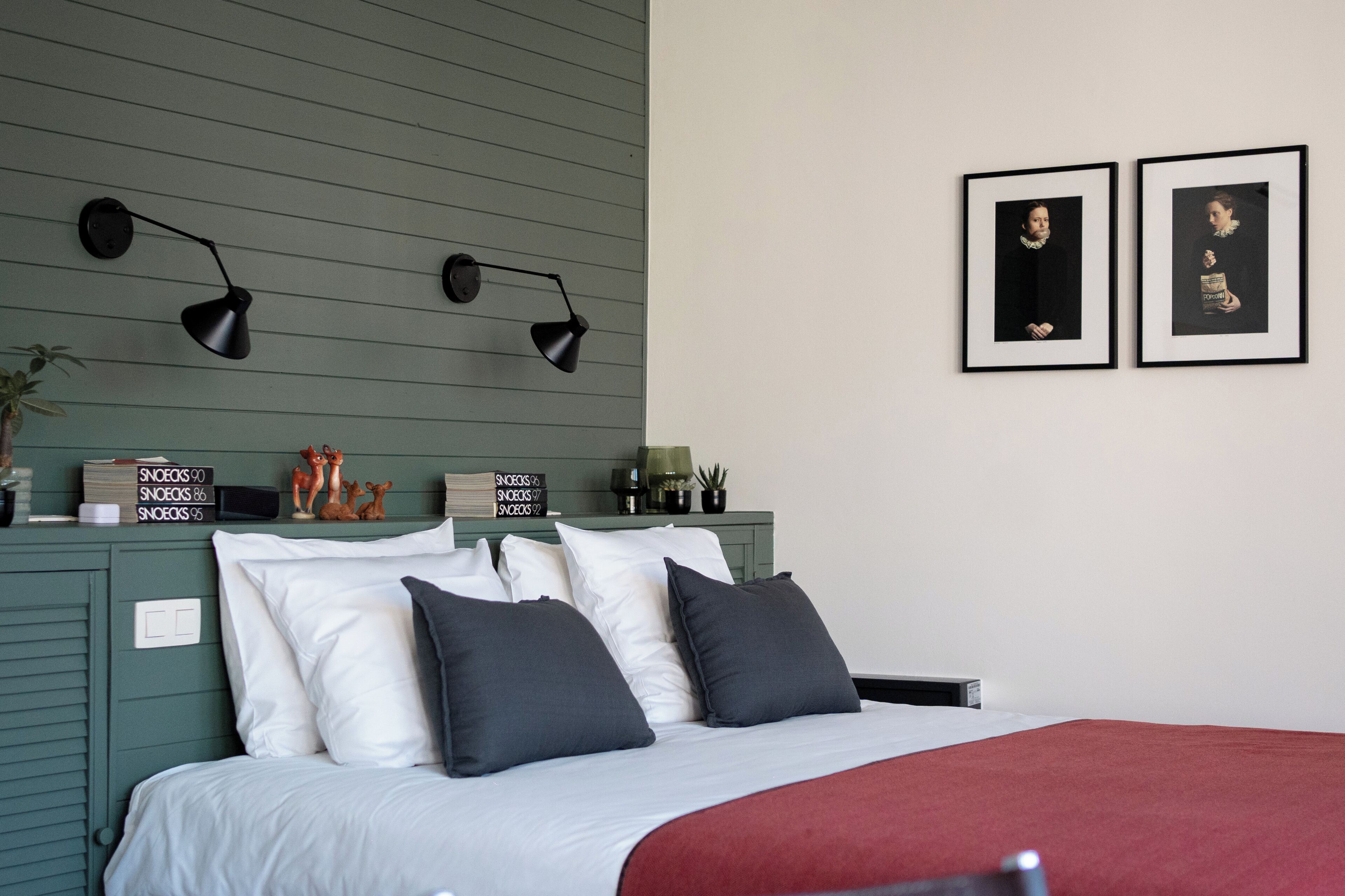 Un dormitorio con una cama, almohadas, un edredón rojo, lámparas de pared y dos cuadros enmarcados.