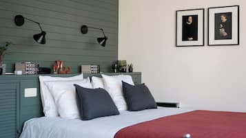 Un dormitorio con una cama, almohadas, un edredón rojo, lámparas de pared y dos cuadros enmarcados.